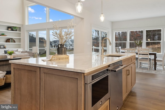 kitchen with a healthy amount of sunlight, an island with sink, a sink, and wood finished floors