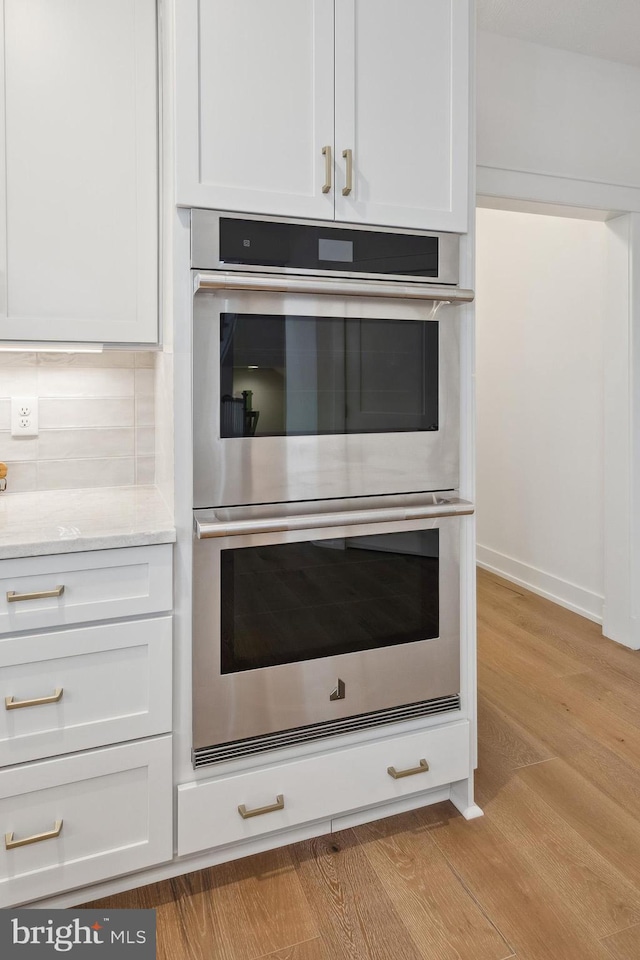 interior space featuring double oven, white cabinets, light wood-type flooring, and light stone countertops