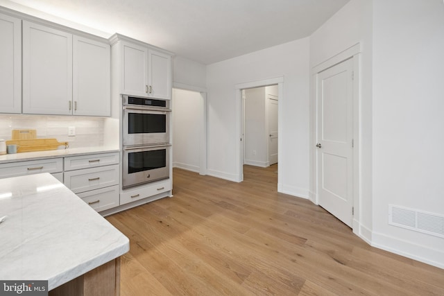 kitchen with stainless steel double oven, light countertops, visible vents, and light wood-style floors
