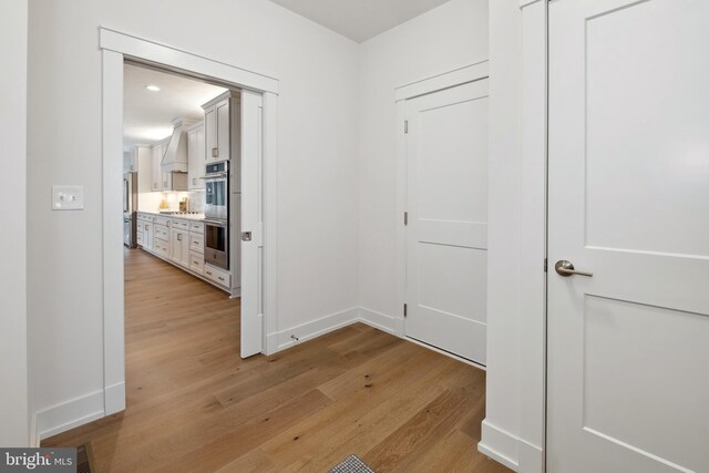 hallway featuring light wood finished floors and baseboards