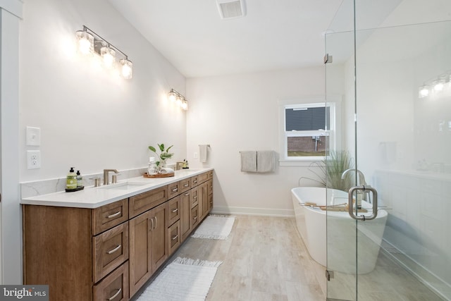 full bath featuring a sink, wood finished floors, visible vents, double vanity, and a freestanding tub