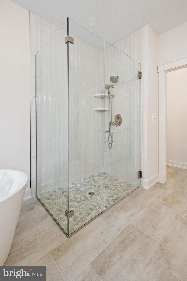full bath with baseboards, a shower stall, and a freestanding tub