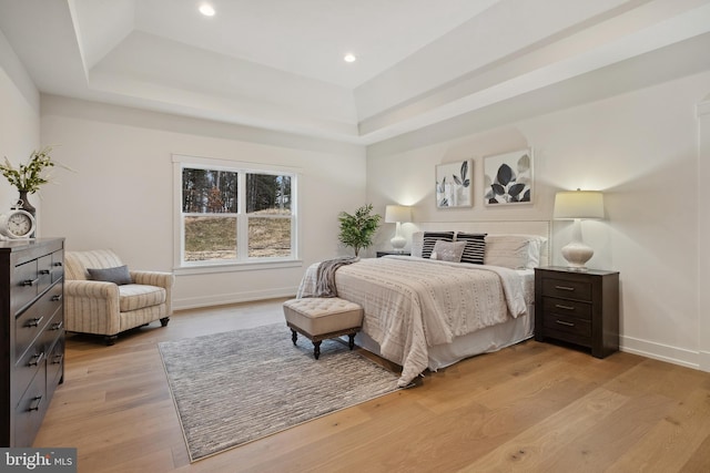 bedroom with baseboards, light wood finished floors, a tray ceiling, and recessed lighting