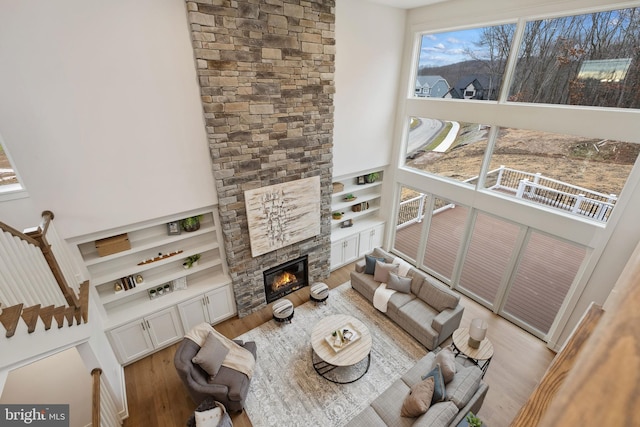 living room featuring built in shelves, a high ceiling, a stone fireplace, and wood finished floors