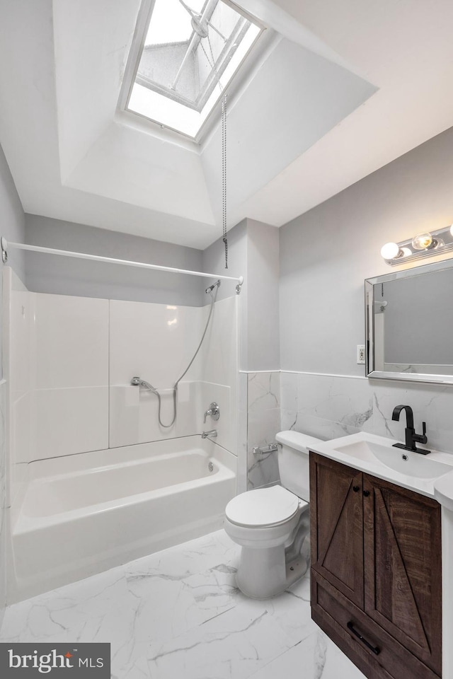 bathroom featuring vanity, toilet, marble finish floor, a skylight, and washtub / shower combination