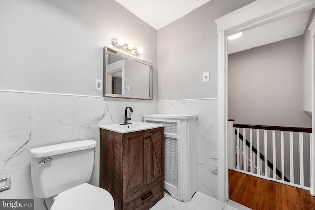 bathroom featuring vanity, tile walls, toilet, marble finish floor, and a wainscoted wall