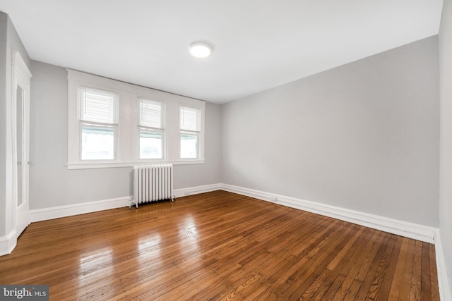 unfurnished room featuring radiator heating unit, hardwood / wood-style floors, and baseboards