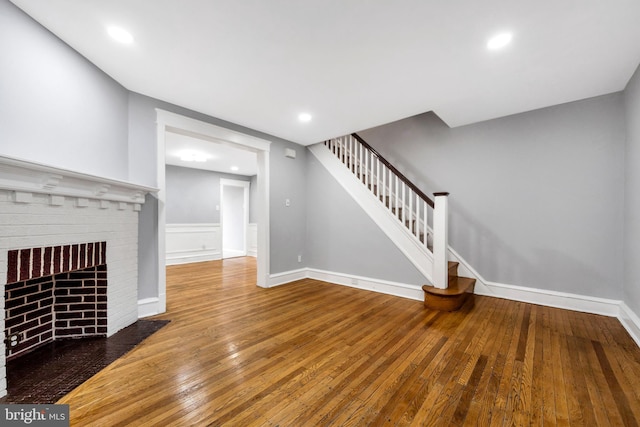 unfurnished living room with stairway, recessed lighting, wood-type flooring, baseboards, and a brick fireplace