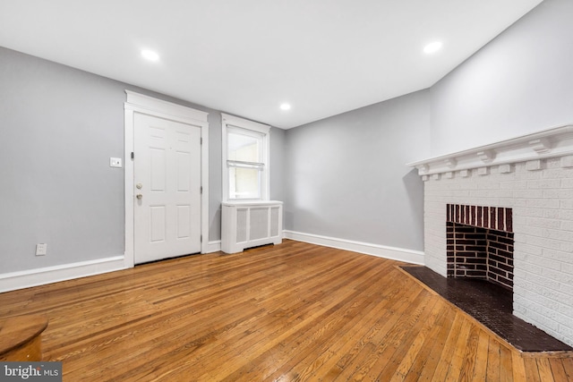 unfurnished living room with wood-type flooring, a brick fireplace, baseboards, and recessed lighting