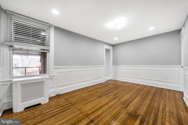 spare room with a wainscoted wall, radiator, recessed lighting, and wood-type flooring