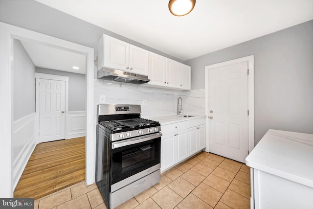 kitchen with a sink, under cabinet range hood, white cabinetry, and stainless steel gas stove