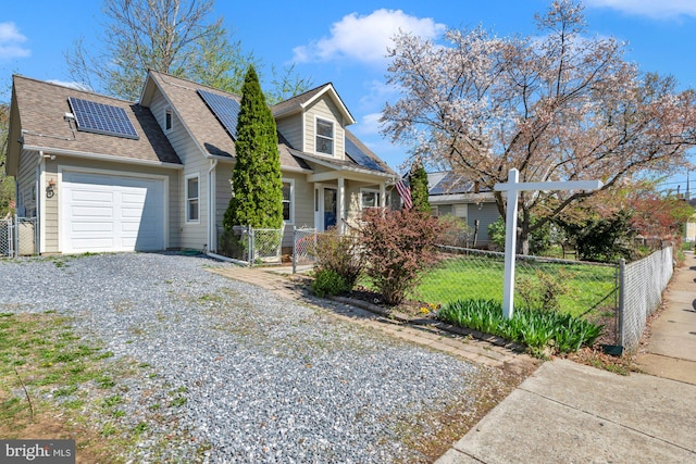 cape cod house featuring driveway, an attached garage, a fenced front yard, a gate, and roof mounted solar panels