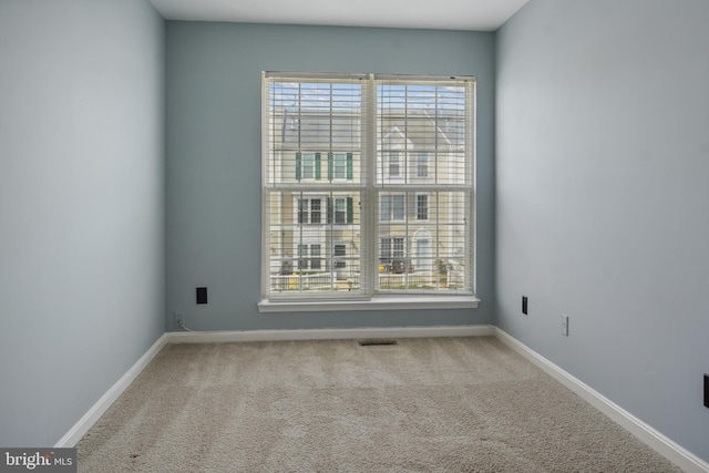 carpeted spare room with baseboards, visible vents, and a healthy amount of sunlight