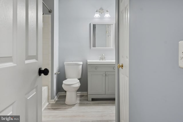 bathroom with wood finished floors, vanity, shower / tub combination, baseboards, and toilet