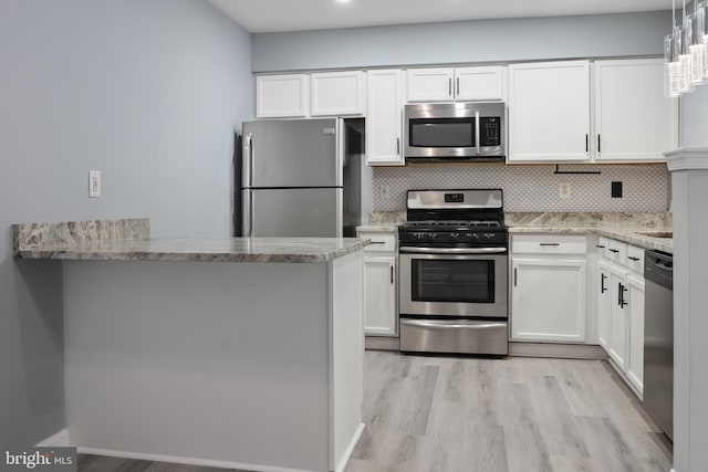 kitchen with a peninsula, backsplash, white cabinetry, light stone counters, and appliances with stainless steel finishes