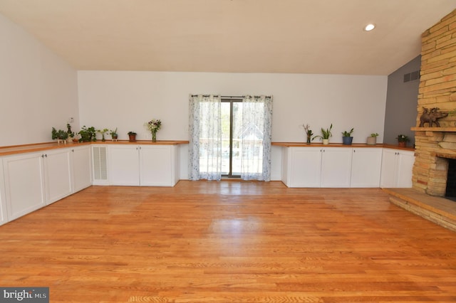 unfurnished living room featuring lofted ceiling, a large fireplace, visible vents, recessed lighting, and light wood finished floors