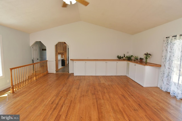 unfurnished room with light wood finished floors, a ceiling fan, arched walkways, and lofted ceiling