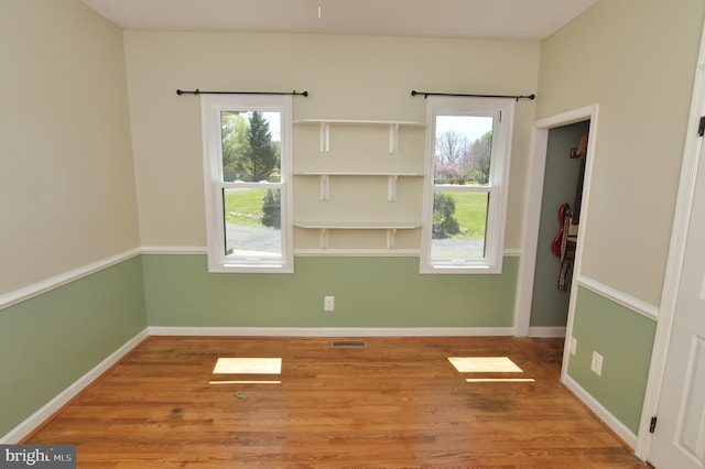spare room with a wealth of natural light, wood finished floors, visible vents, and baseboards