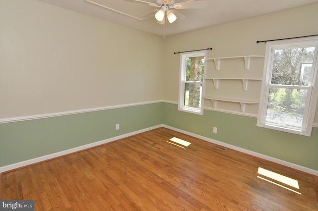 unfurnished room featuring a ceiling fan, visible vents, wood finished floors, and baseboards