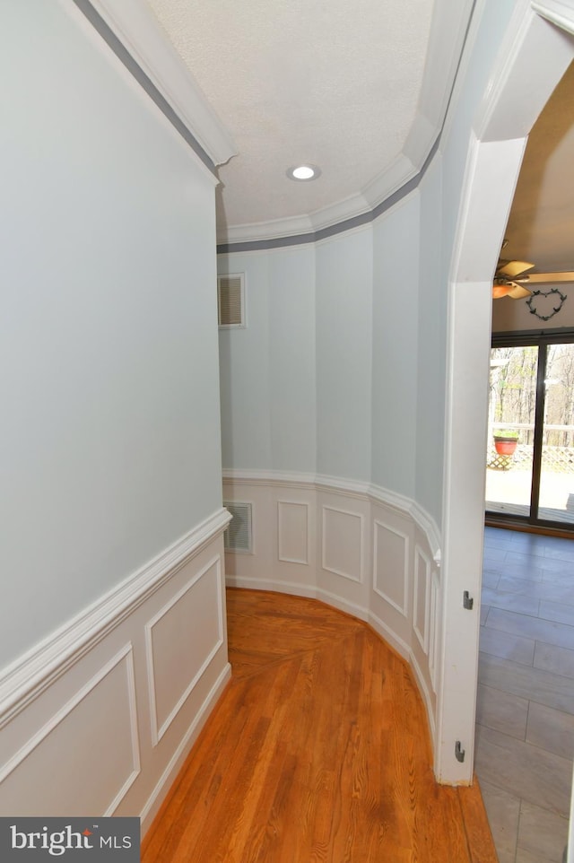 hall with ornamental molding, recessed lighting, a wainscoted wall, and visible vents