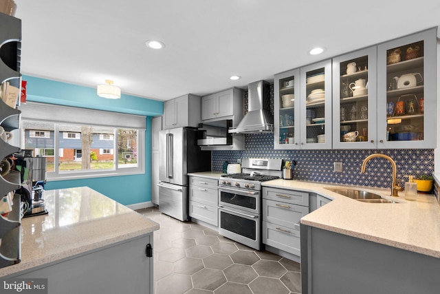 kitchen with wall chimney range hood, gray cabinetry, a sink, and appliances with stainless steel finishes
