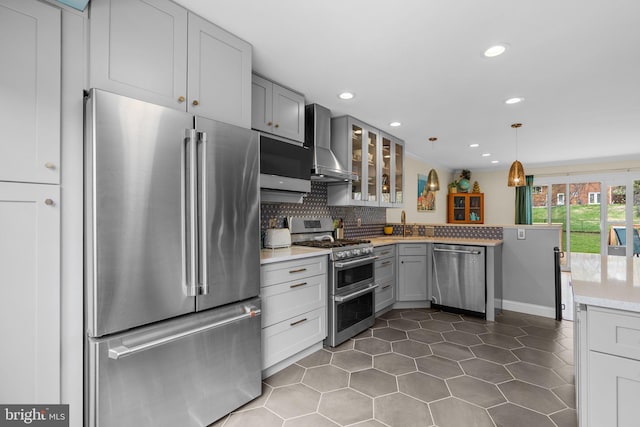 kitchen featuring glass insert cabinets, wall chimney exhaust hood, dark tile patterned floors, gray cabinetry, and stainless steel appliances