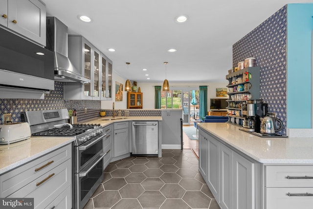 kitchen with wall chimney exhaust hood, a sink, dark tile patterned floors, appliances with stainless steel finishes, and a peninsula