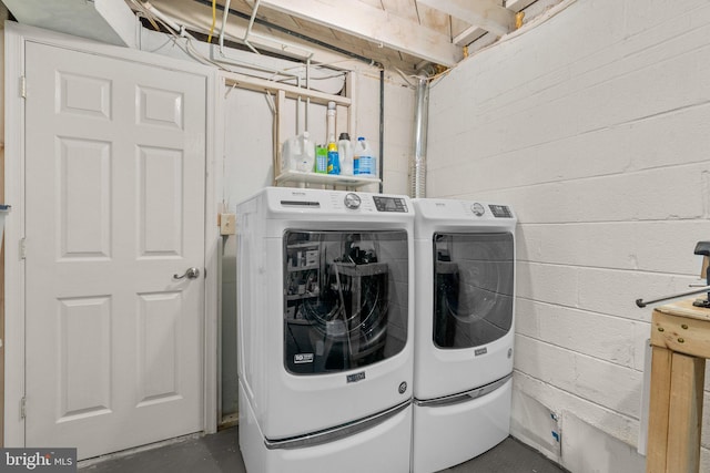 clothes washing area with laundry area, washing machine and clothes dryer, and concrete block wall