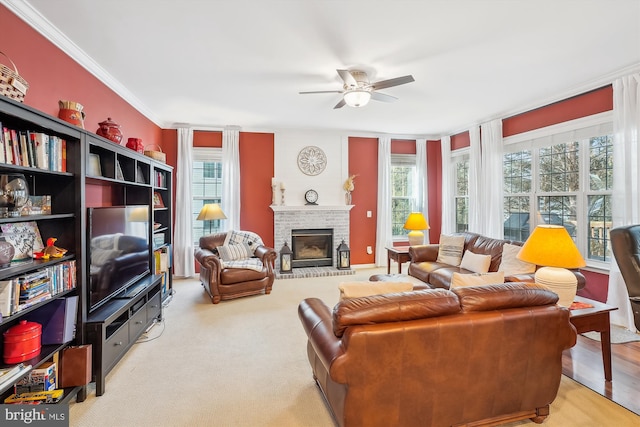 living room with a brick fireplace, ceiling fan, crown molding, and a healthy amount of sunlight