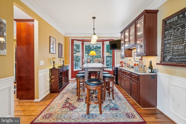 dining room with light wood-style floors, crown molding, and wainscoting
