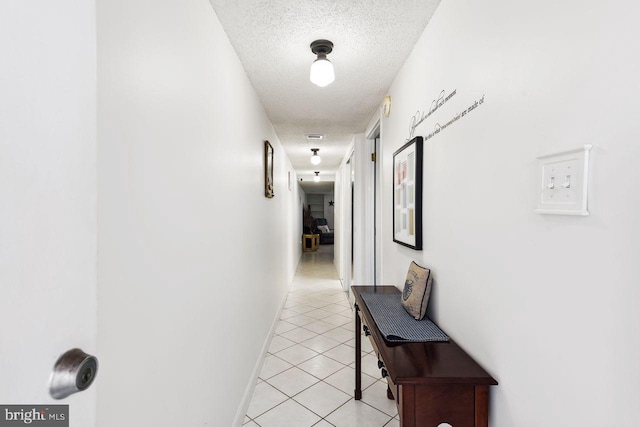 hall featuring a textured ceiling, light tile patterned floors, and baseboards