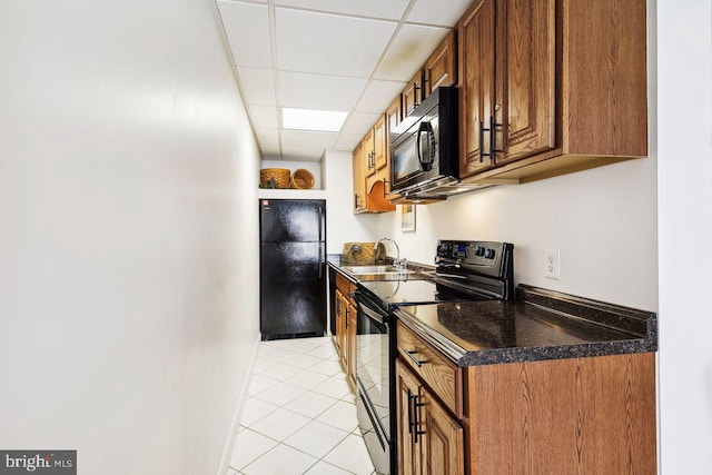 kitchen with a paneled ceiling, light tile patterned floors, black appliances, a sink, and brown cabinets