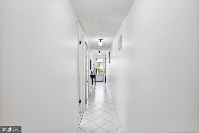 corridor featuring a textured ceiling, light tile patterned floors, and baseboards