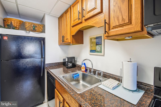 kitchen with a paneled ceiling, black appliances, a sink, dark countertops, and brown cabinets