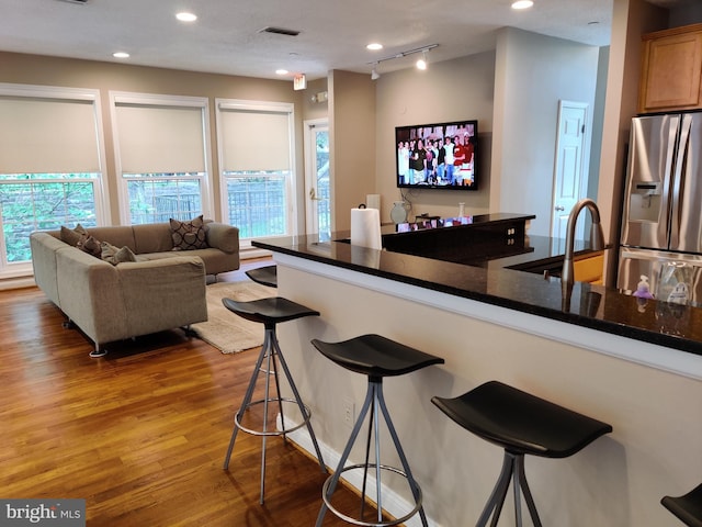 kitchen with stainless steel fridge with ice dispenser, dark countertops, a breakfast bar, wood finished floors, and recessed lighting