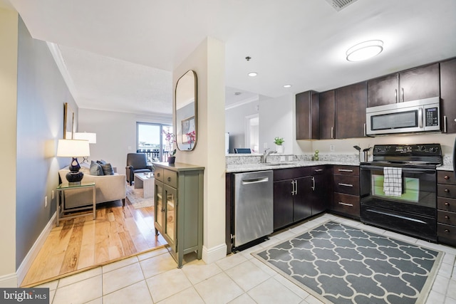 kitchen featuring light tile patterned floors, a sink, open floor plan, appliances with stainless steel finishes, and dark brown cabinets