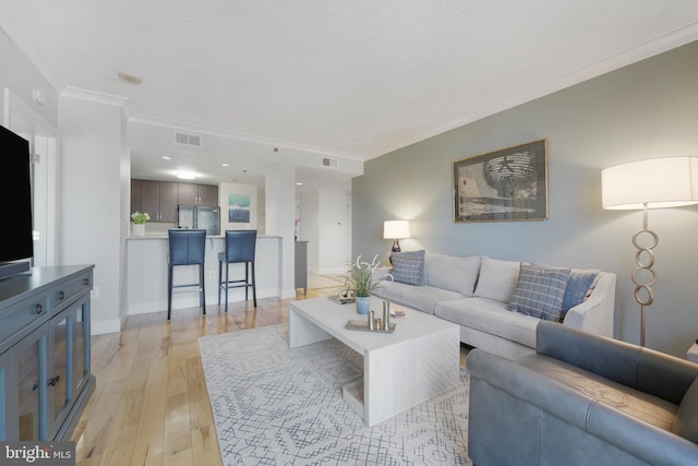 living area with visible vents, baseboards, ornamental molding, light wood-style floors, and a textured ceiling