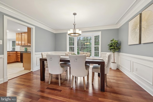 dining space featuring crown molding, a decorative wall, wood finished floors, wainscoting, and a notable chandelier
