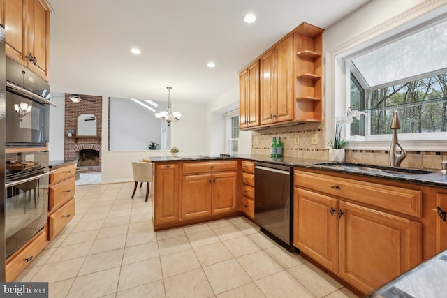 kitchen featuring dishwashing machine, a peninsula, a sink, a brick fireplace, and a notable chandelier