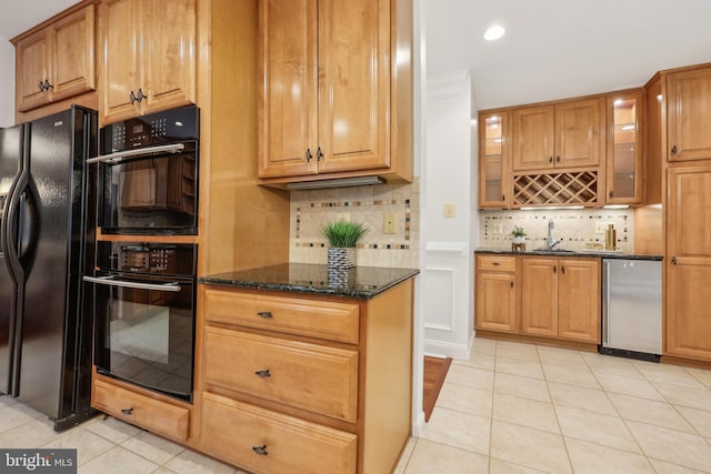 kitchen featuring glass insert cabinets, backsplash, light tile patterned flooring, dark stone counters, and black appliances