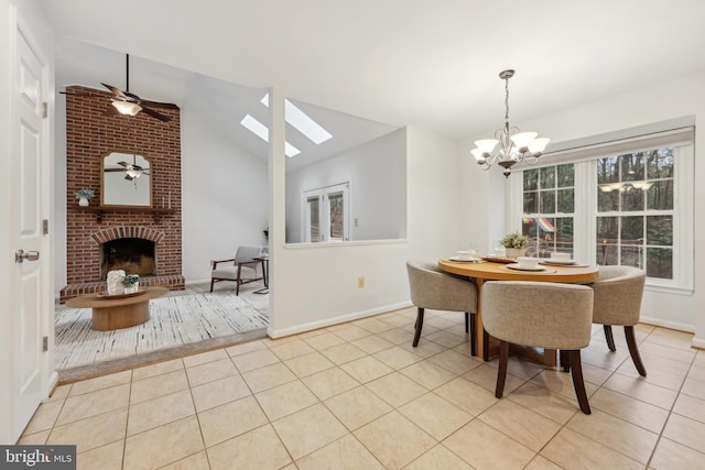 dining space with vaulted ceiling with skylight, ceiling fan with notable chandelier, light tile patterned floors, a fireplace, and baseboards