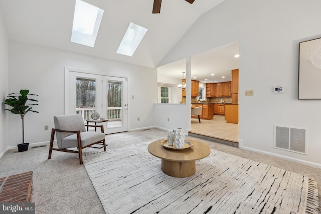 sitting room with visible vents, baseboards, a skylight, high vaulted ceiling, and light carpet