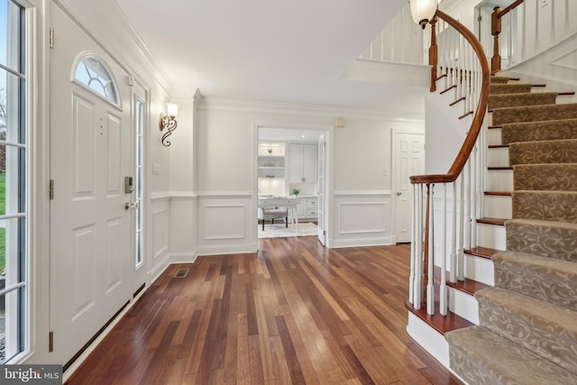 foyer entrance with stairs, wood-type flooring, ornamental molding, and a decorative wall