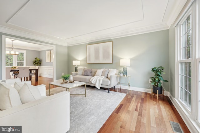 living area with baseboards, light wood-type flooring, ornamental molding, a chandelier, and visible vents
