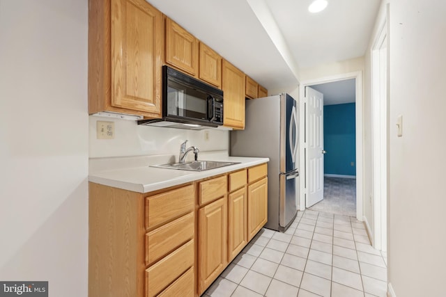 kitchen with black microwave, light countertops, freestanding refrigerator, light tile patterned flooring, and a sink