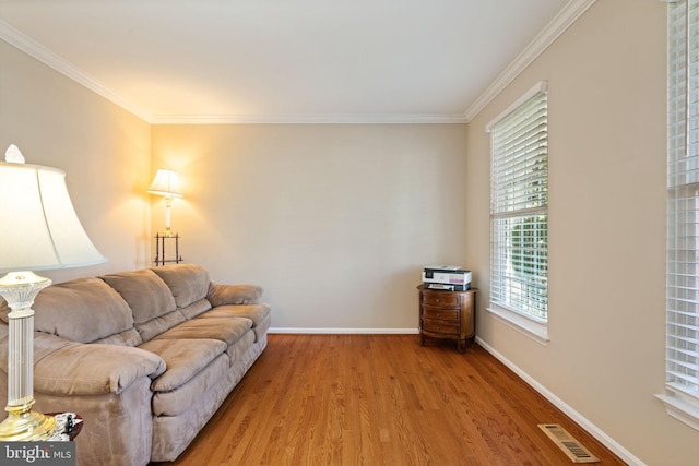 living area with baseboards, ornamental molding, light wood finished floors, and visible vents