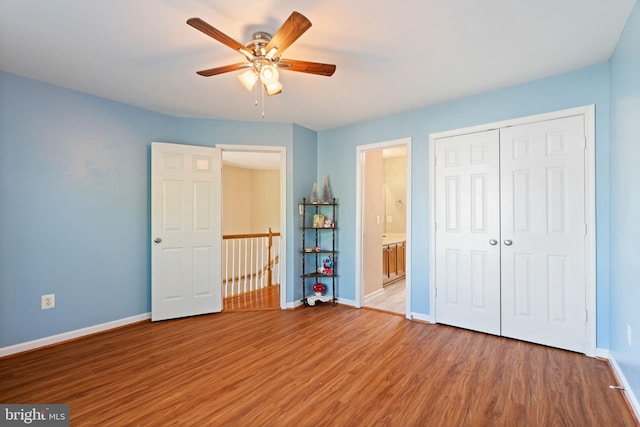 unfurnished bedroom featuring wood finished floors, a closet, ceiling fan, baseboards, and ensuite bath