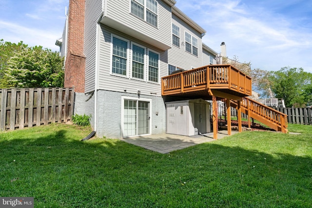 rear view of property featuring brick siding, a wooden deck, fence, and a lawn
