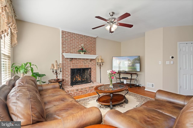living area featuring ceiling fan, a brick fireplace, wood finished floors, and visible vents