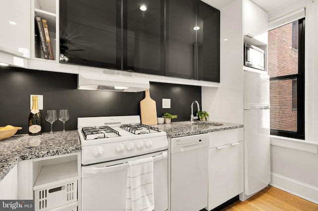 kitchen with white appliances, light wood-style floors, white cabinetry, under cabinet range hood, and a sink